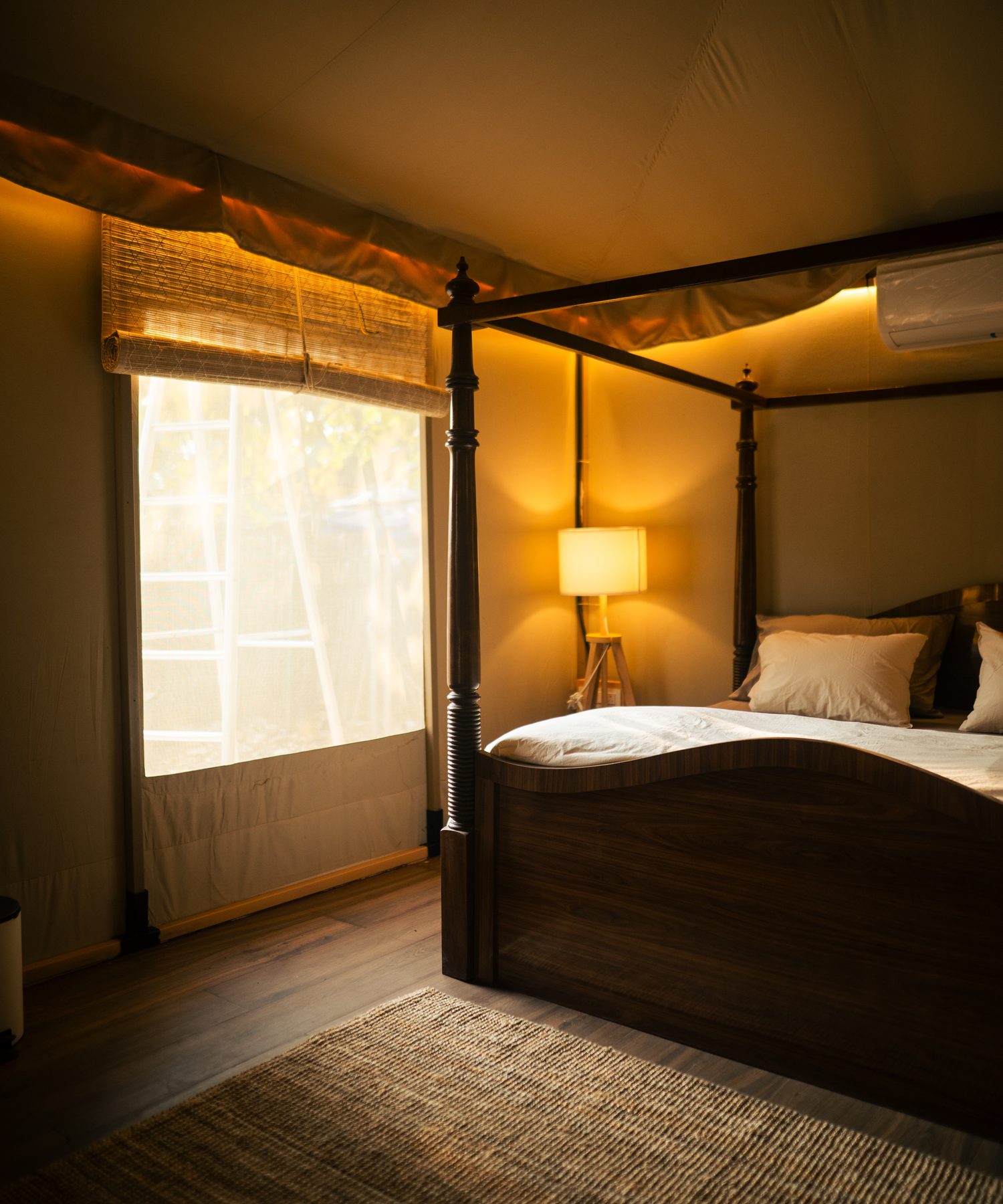 a four-poster bed against the canvas wall, blind half-drawn