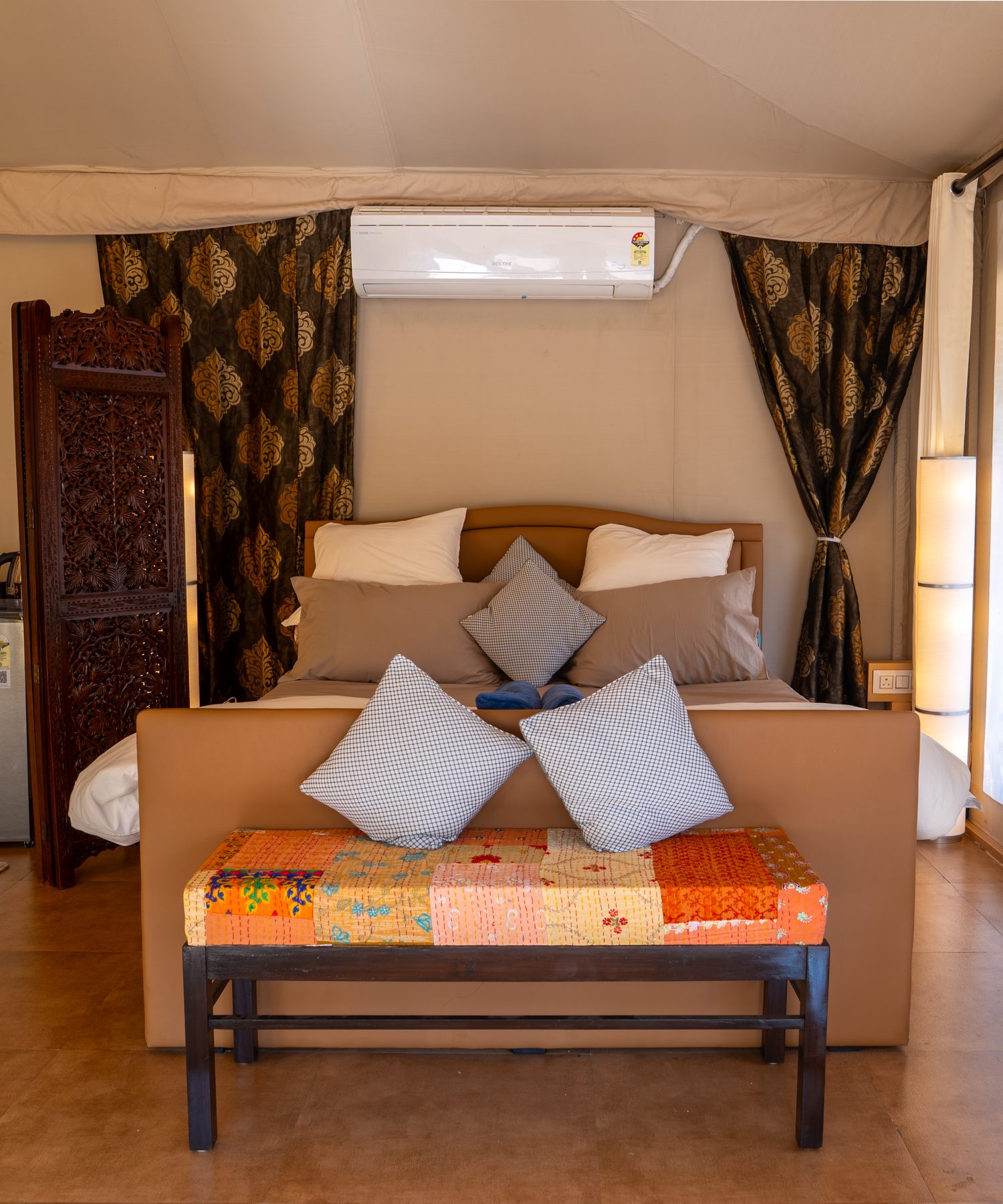 the king bed, carved screen behind it and a quilted bench at its foot