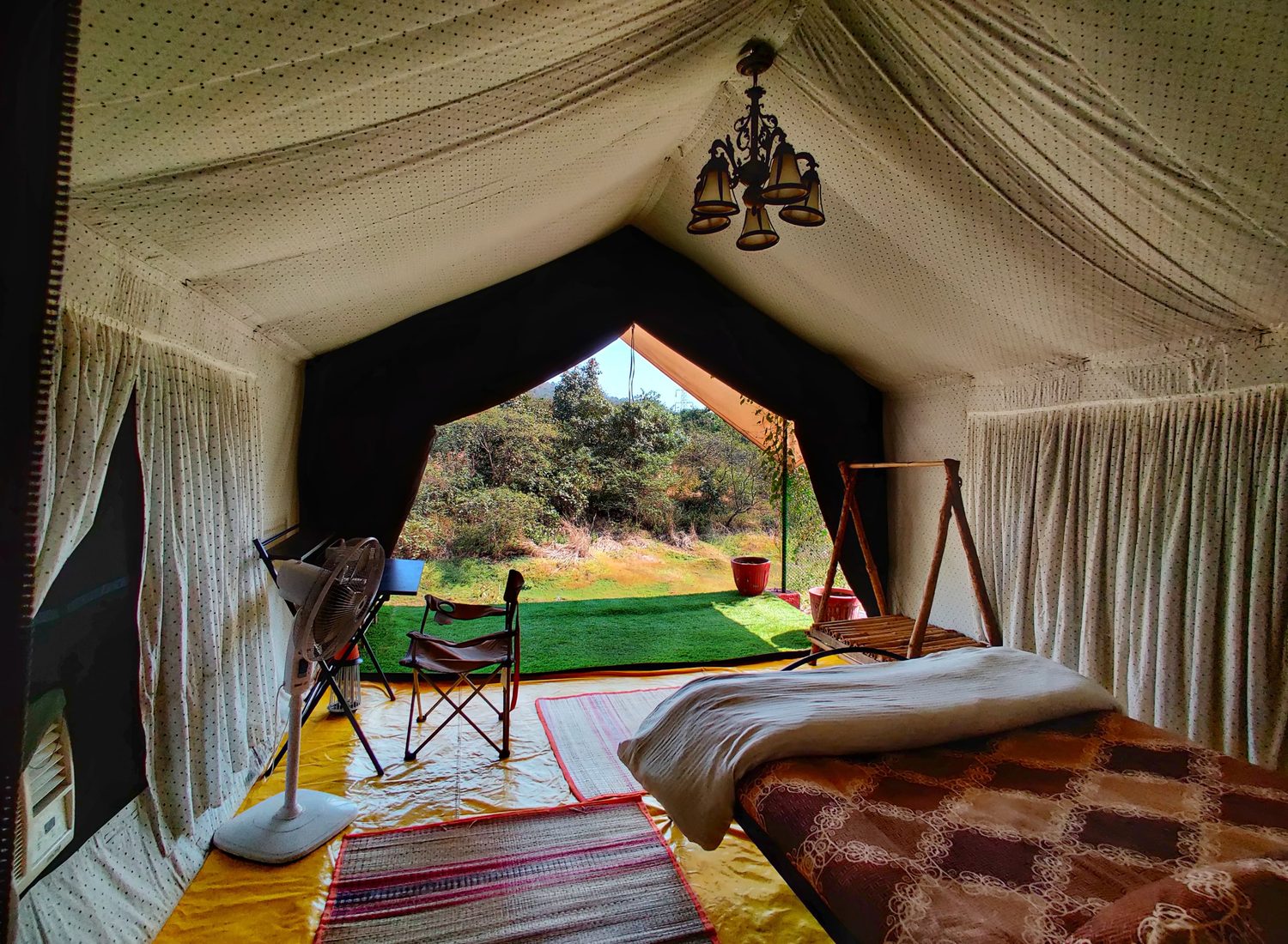 the bed under a chandelier, canvas drapes pulled back to the view